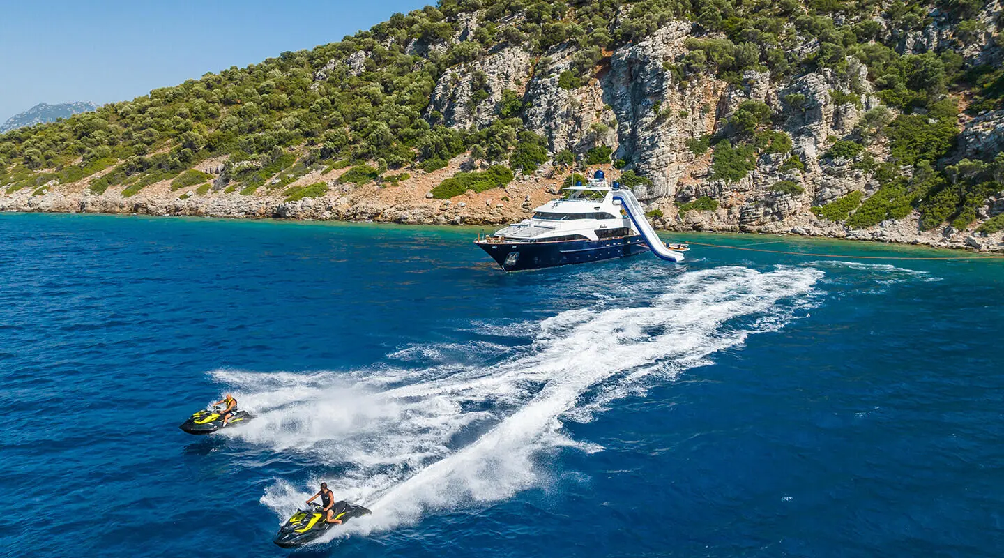 Amadea yacht cruising blue water near rocky coastline with wake