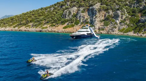 Amadea yacht cruising blue water near rocky coastline with wake