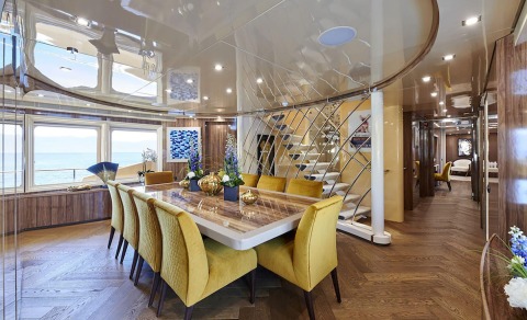 Daloli yacht interior: luxurious dining salon with a long marble table, yellow upholstered chairs, and panoramic ocean views through large windows
