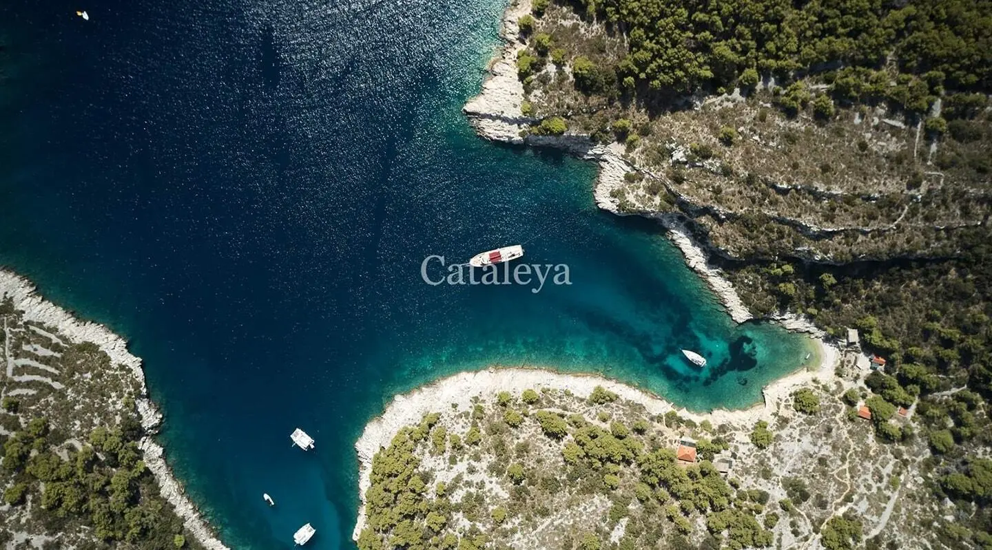 Aerial view of a yacht in turquoise waters by rocky coastline