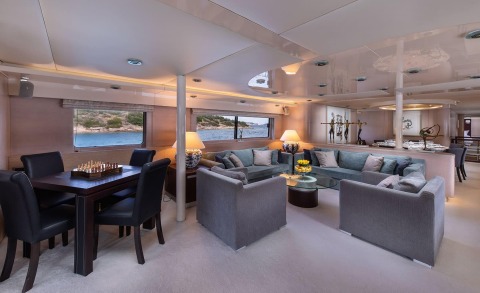 Interior of Magix yacht with seating area and dining table, view of sea through windows