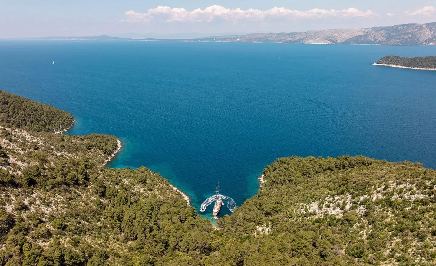 Dalmatino yacht anchored along rocky coastline with blue sea backdrop