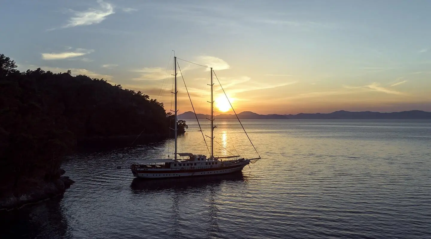 Sunset over calm water with a small gulet anchored near rocky shore, Tersane 8