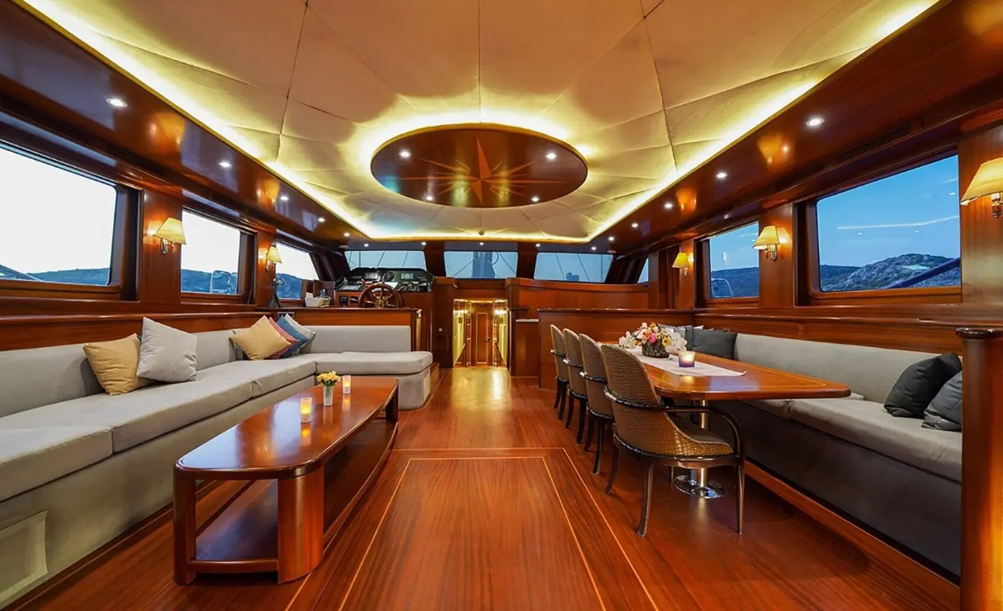Inside La Bella Vita yacht: polished wooden deck, seating, helm, and dining area under warm lighting