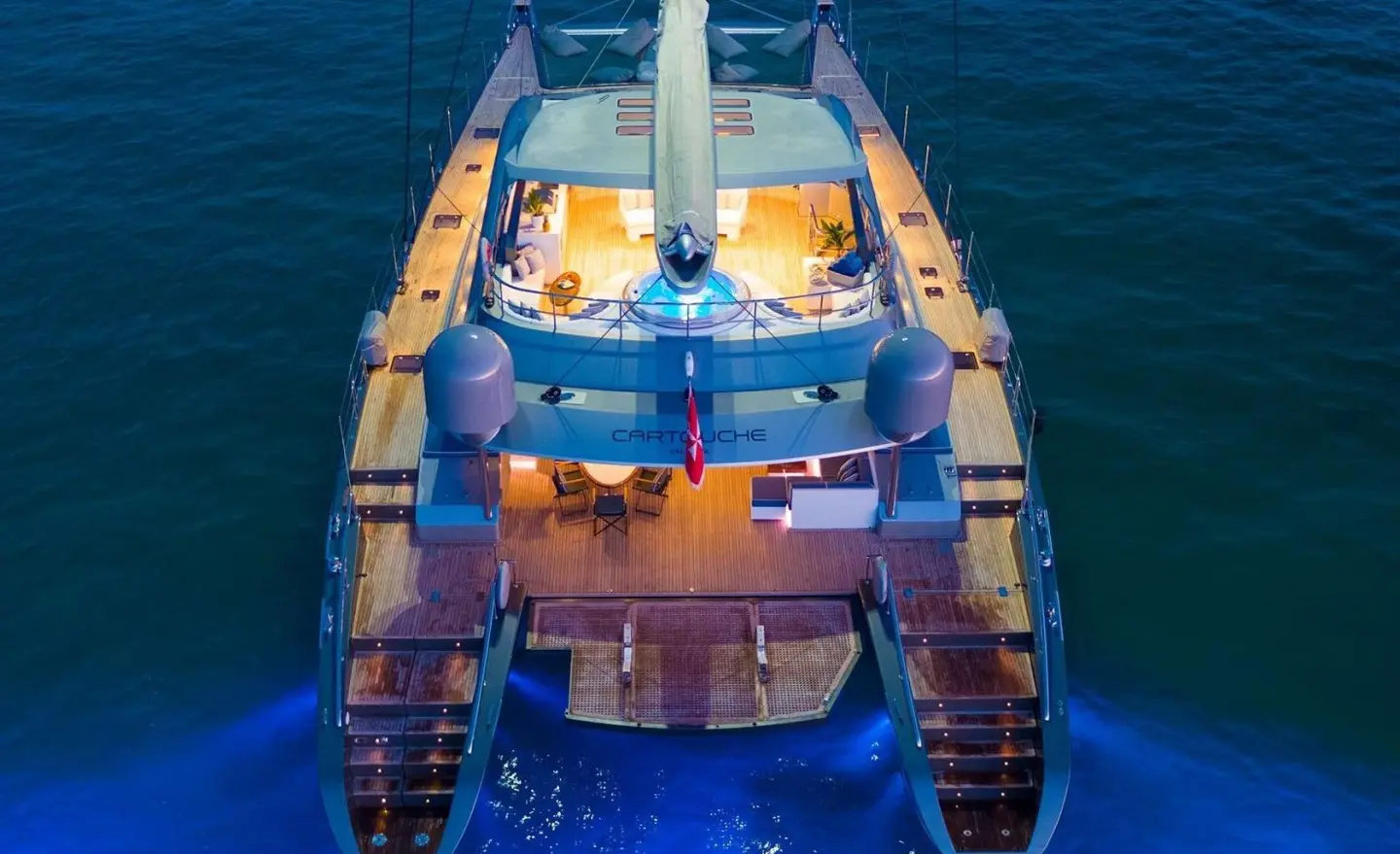 Cartouche yacht seen from above at sea, sunlit deck, lifebuoys visible