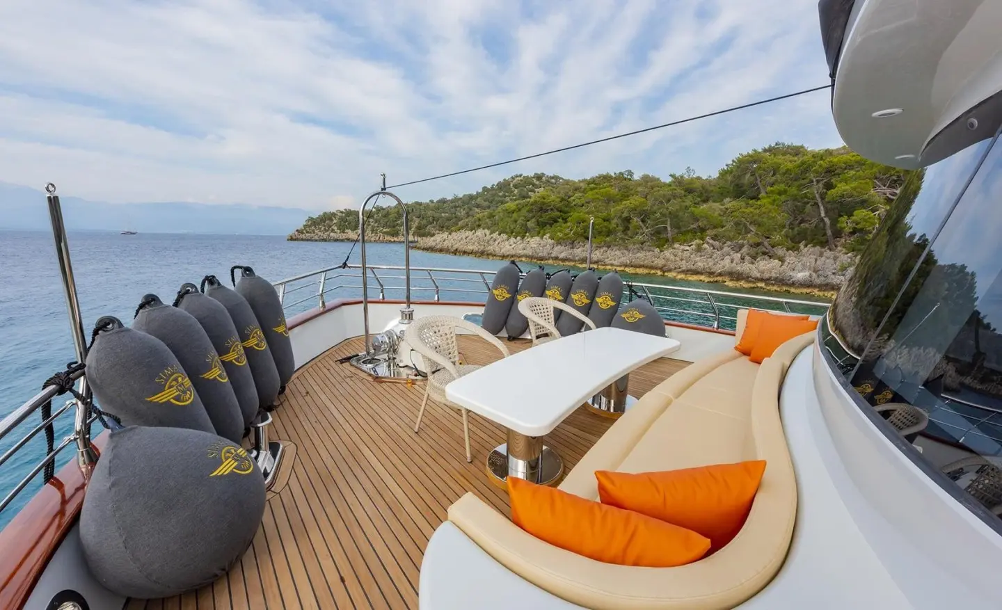 Simay M motor yacht deck with orange cushions, seating, and sunny coastal backdrop