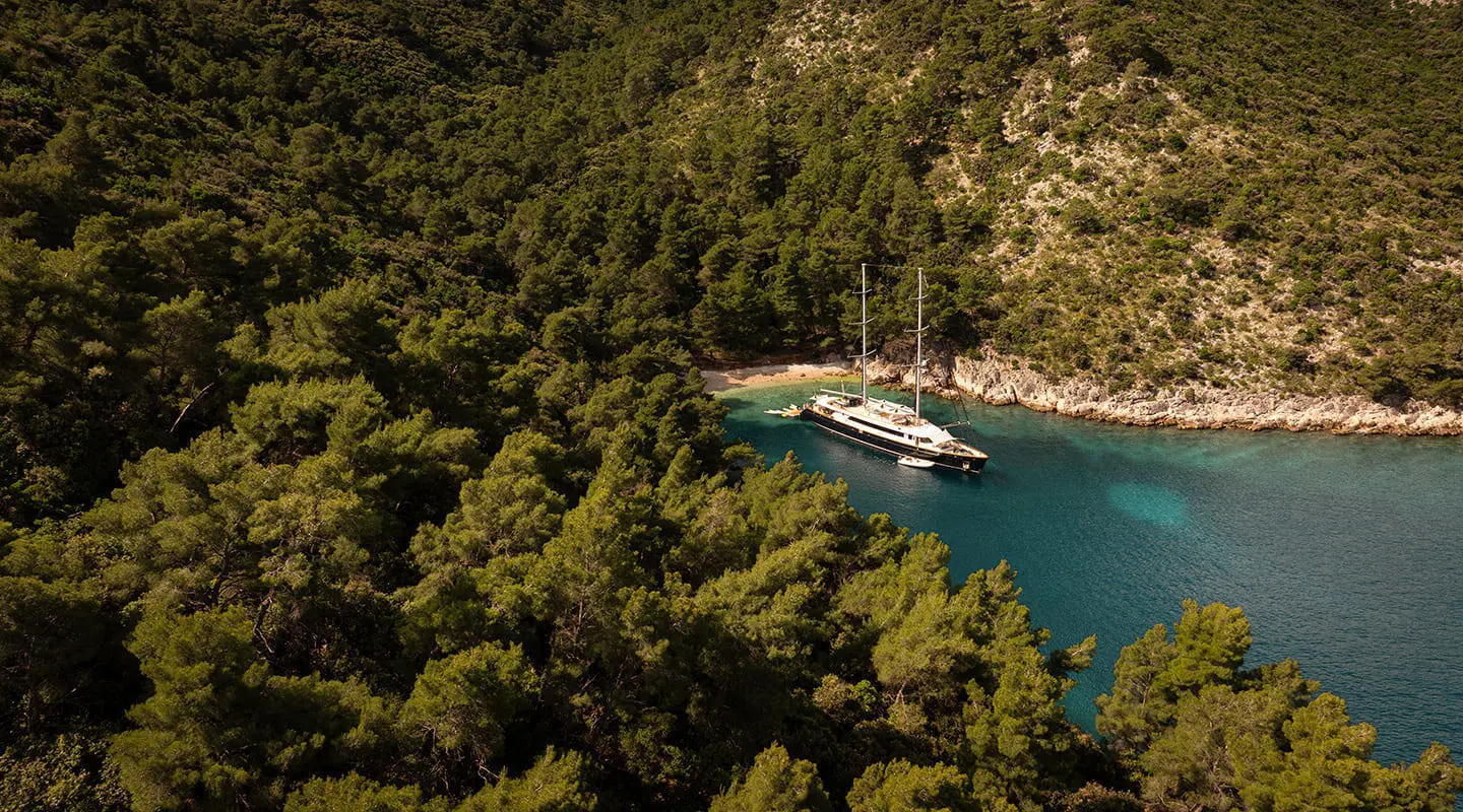Yacht Dalmatino anchored in a turquoise cove surrounded by rocky cliffs