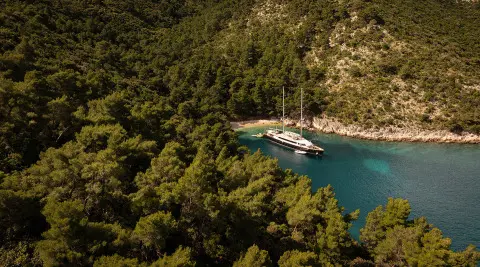 Yacht Dalmatino anchored in a turquoise cove surrounded by rocky cliffs