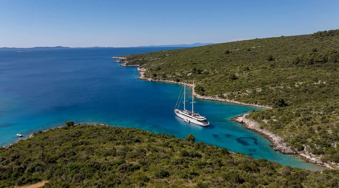 Yacht Anima Maris anchored along a rugged coastline with clear blue sea