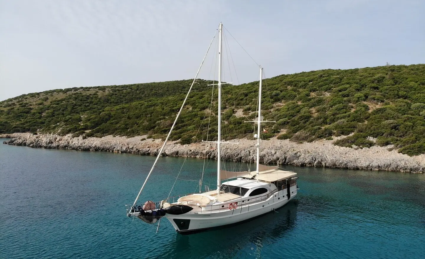 Anchored luxury sailing yacht beside rocky shoreline