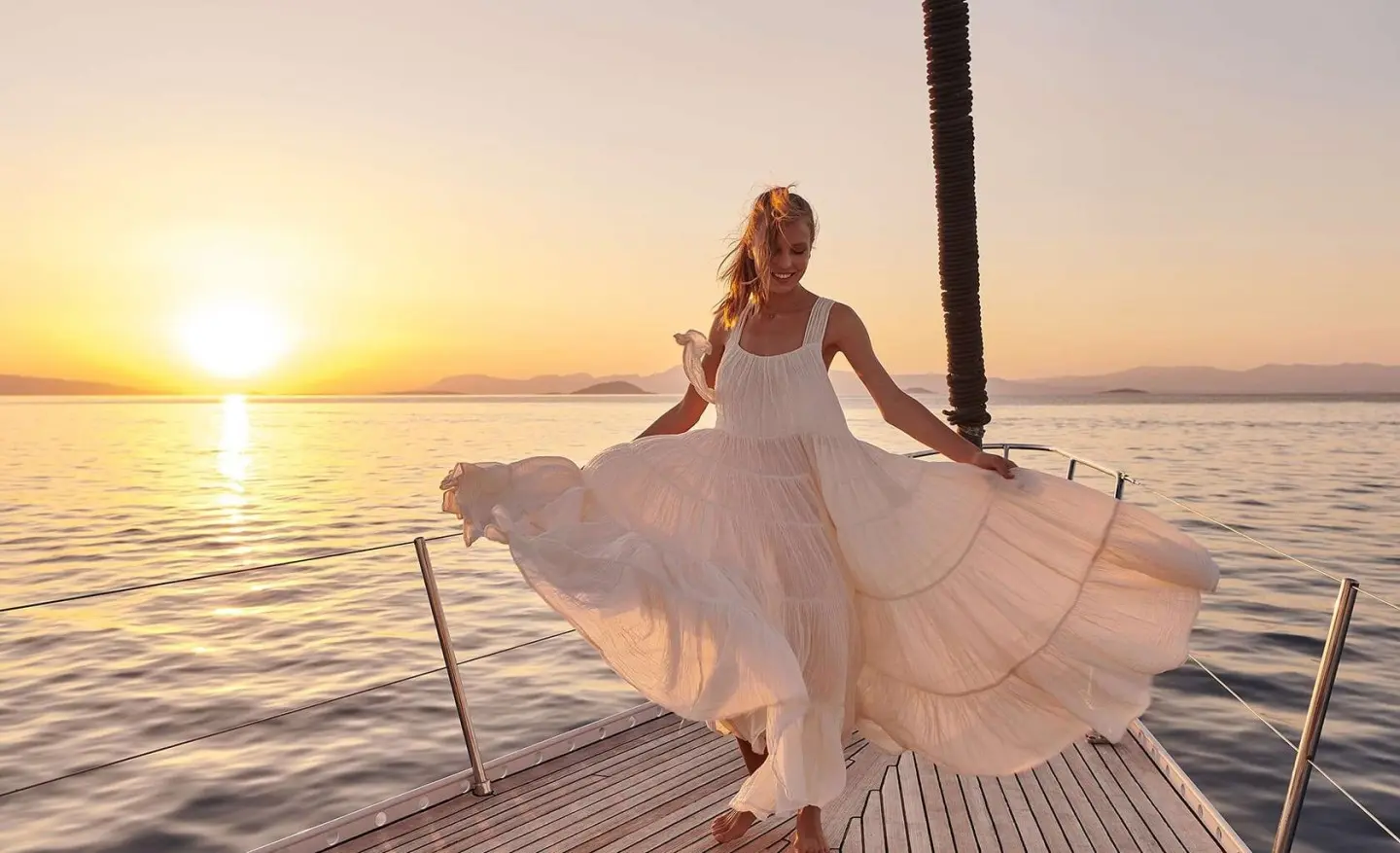Sunset on the Aizu yacht deck with a flowing white dress, railing, and calm sea