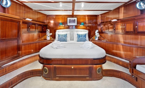 Smart Spirit cabin interior with polished wood panels, central queen bed, blue accents, and brass portholes