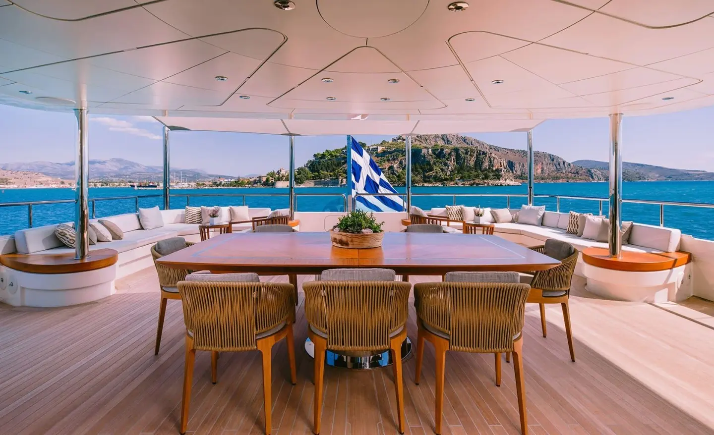 Xana luxury yacht dining area with wooden table and chairs on deck at sunset