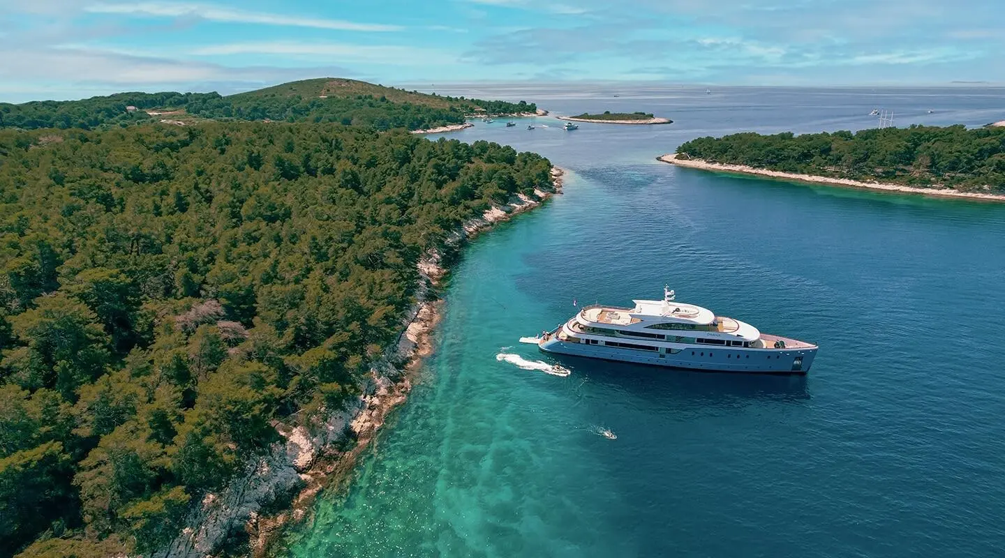 Ohana luxury yacht anchored near a lush green coastline and clear turquoise water