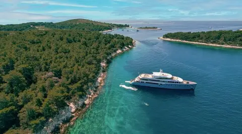 Ohana luxury yacht anchored near a lush green coastline and clear turquoise water