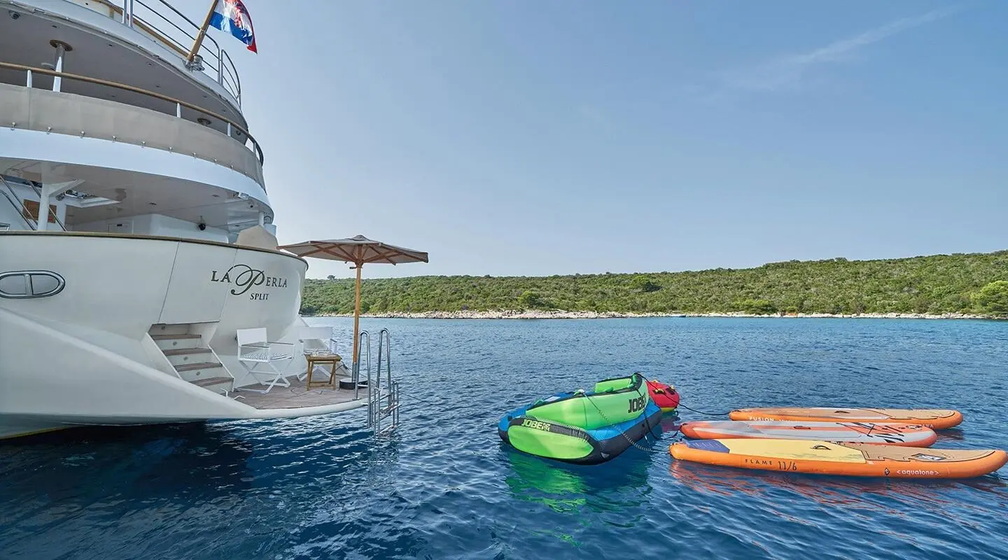 La Perla yacht moored by turquoise water with colorful kayaks near stern