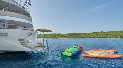 La Perla yacht moored by turquoise water with colorful kayaks near stern