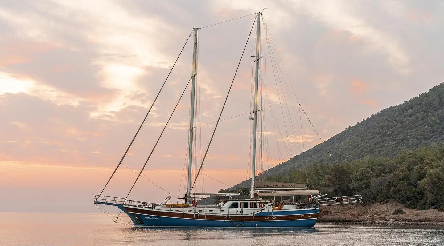 Gozdem The One yacht anchored near a hillside at sunset with sails down