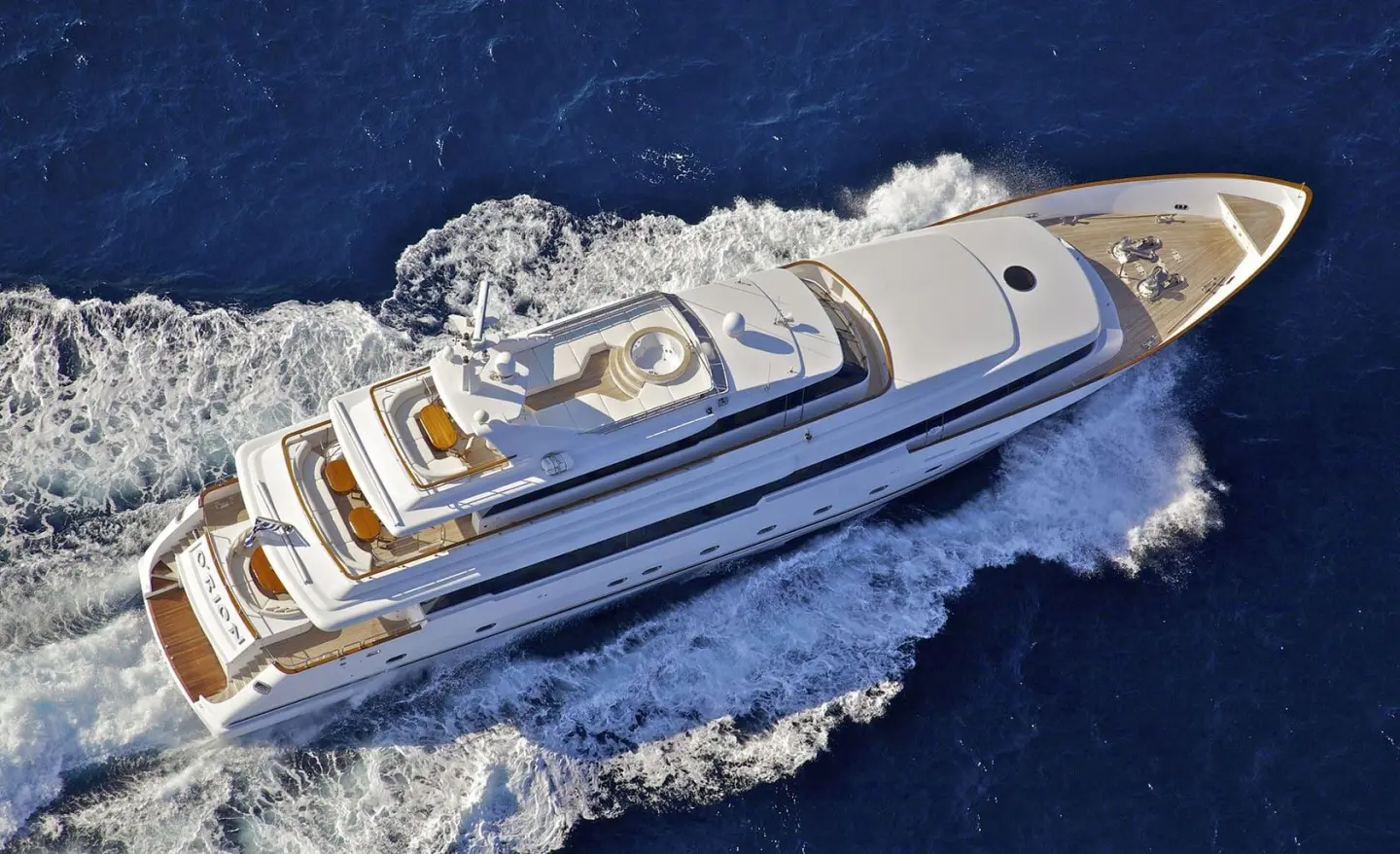 Aerial view of a sleek white yacht cutting through blue sea, wake trailing
