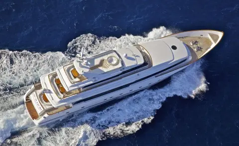Aerial view of a sleek white yacht cutting through blue sea, wake trailing