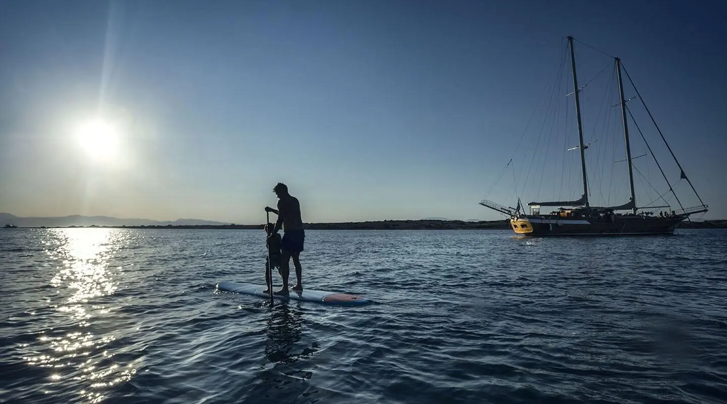 Two people stand on a calm blue sea at sunset aboard a yacht, Entre Cielos.