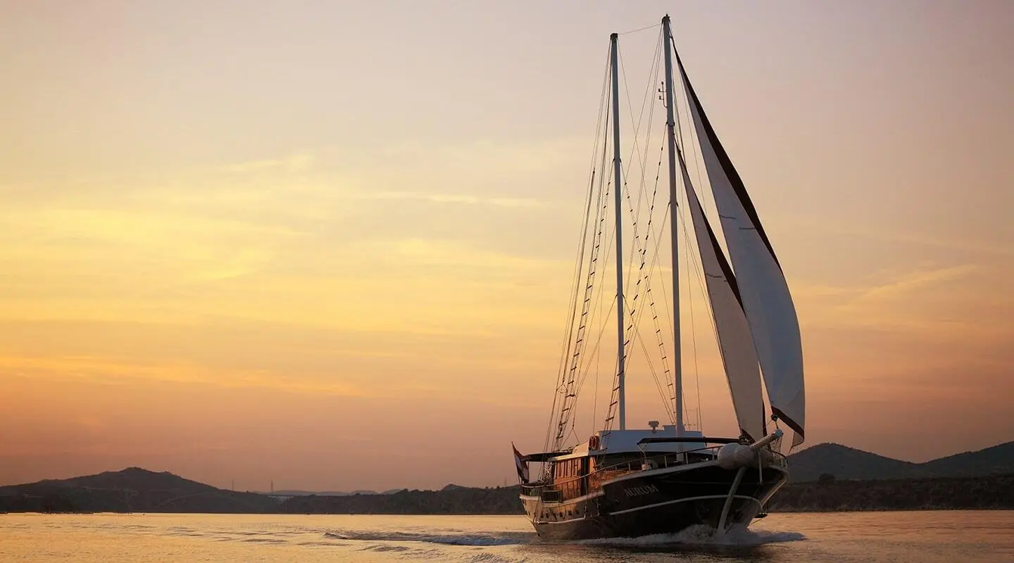 A sunset-lit luxury gulet yacht named Aurum docked by calm water.
