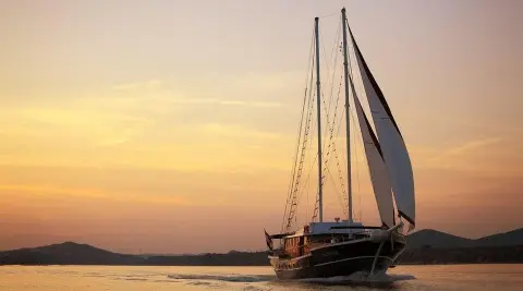 A sunset-lit luxury gulet yacht named Aurum docked by calm water.
