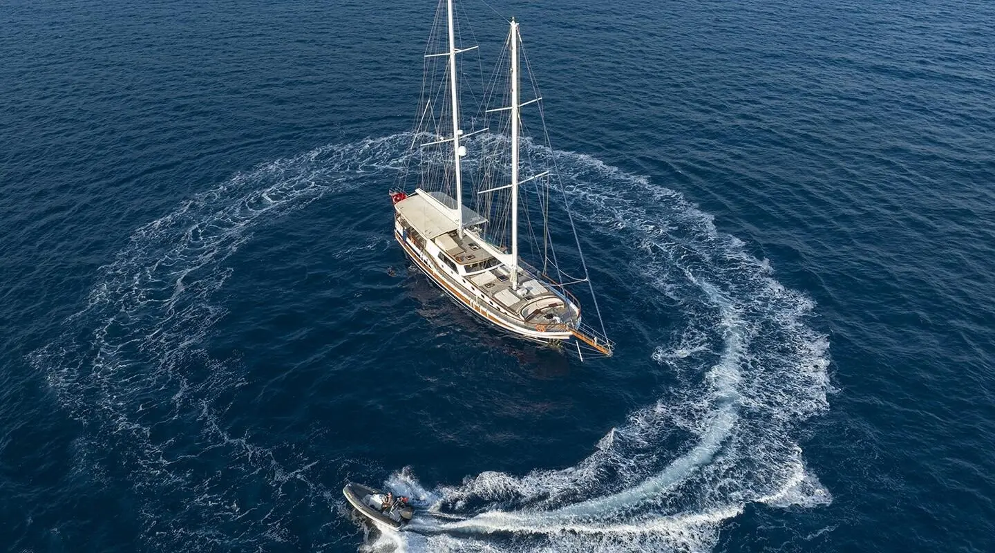 A luxury sailing yacht Artemis glides on deep blue water at sunset, sails lowered