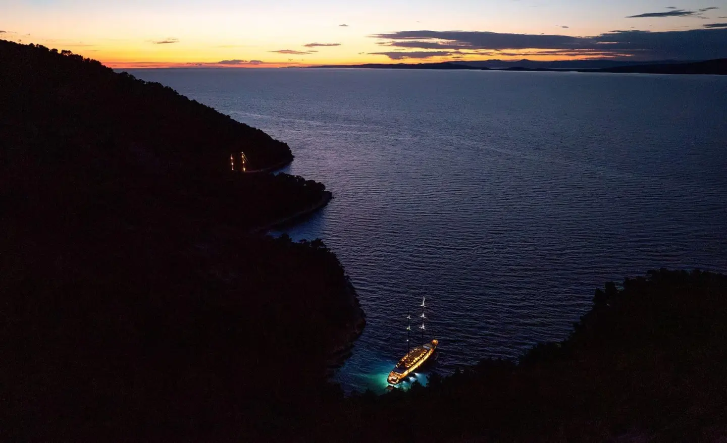 Dalmatino yacht silhouette at sunset along rocky coastline and calm sea