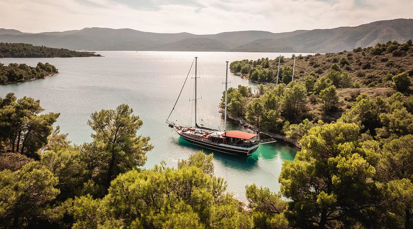 Two-masted wooden gulet anchored in calm turquoise bay among trees