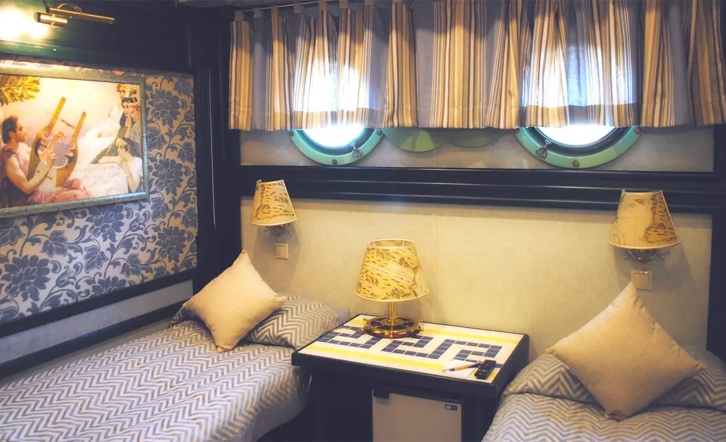Interior yacht cabin with two beds, lamps, and cushions by a window