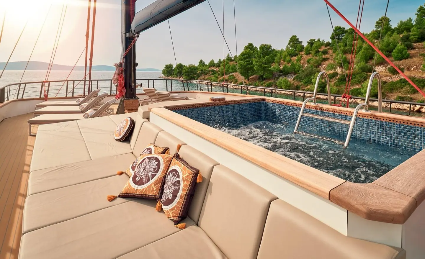 Deck of Anetta yacht with beige seating, cushions, and a view of the pool and treeline