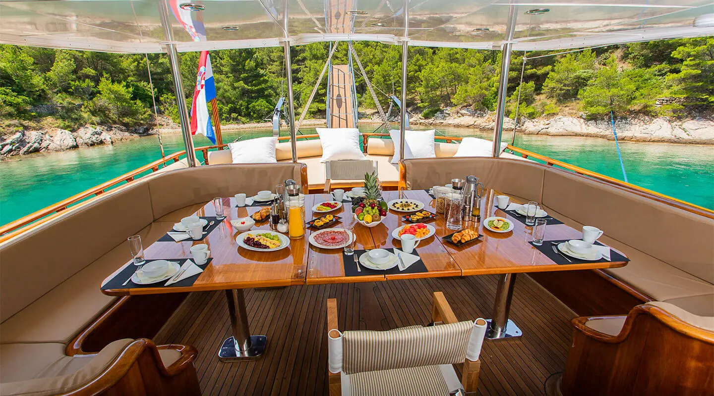 Dolce Vita yacht dining setup on deck with food and chairs at sunrise on a luxury gulet