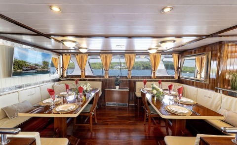 Cesarica dining salon onboard luxury yacht with wood panels, cream seating, and large windows framed by orange curtains