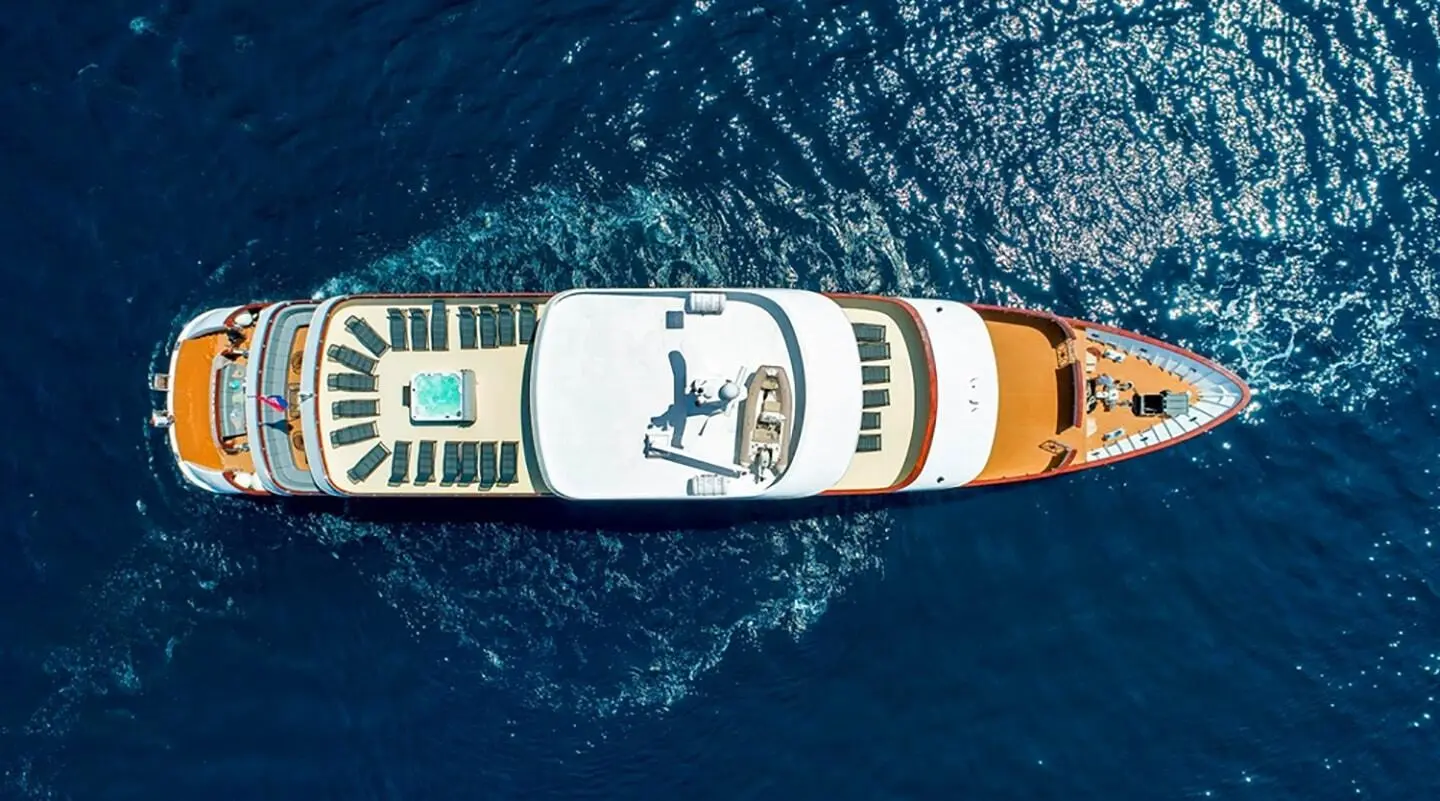 Aerial view of a luxury yacht named Yolo cruising blue ocean at dusk