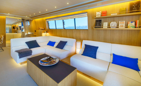 Phantom yacht interior with white sectional sofas, wooden walls, shelves, and windows