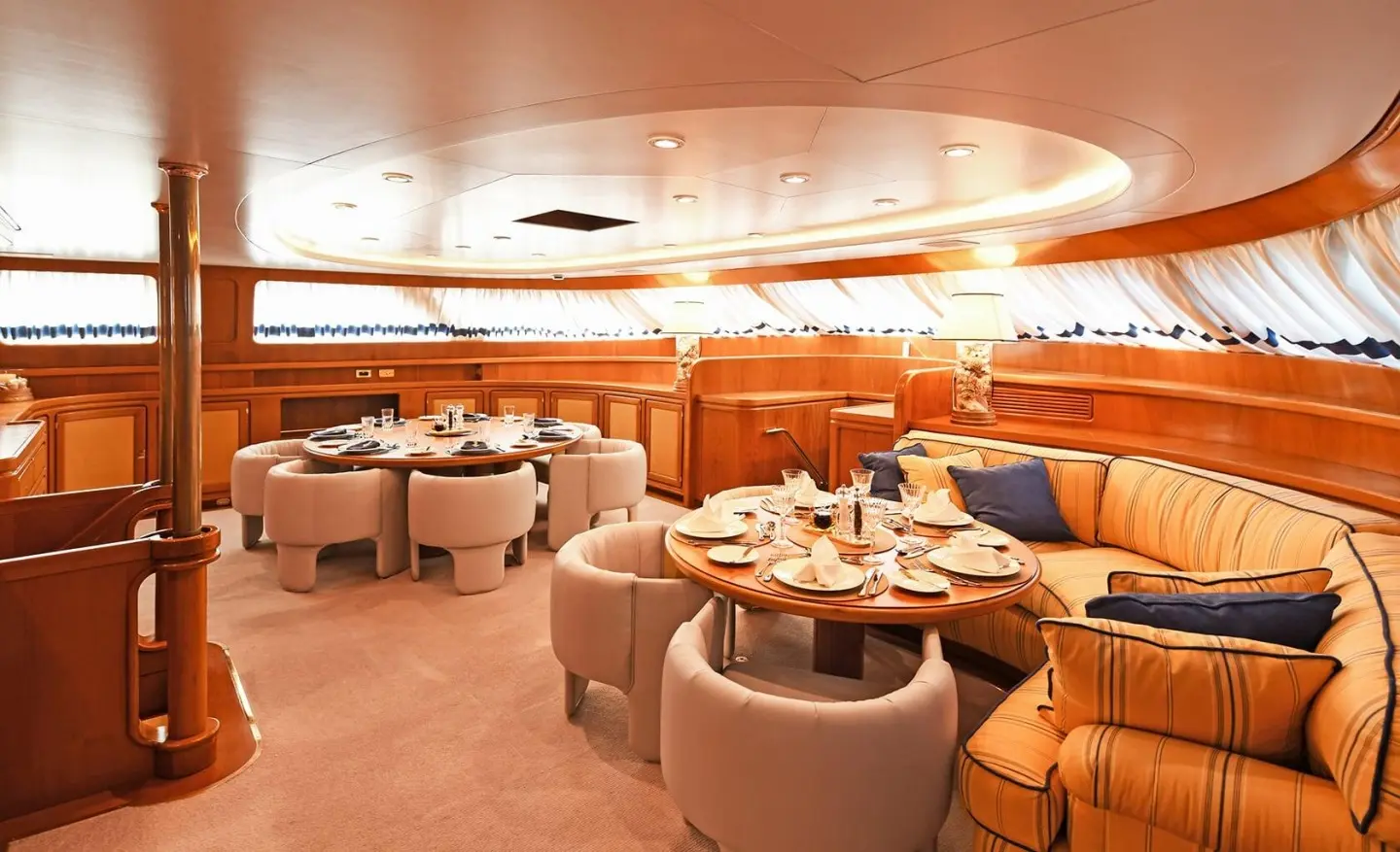 Inside Tamarita yacht saloon with beige seating, wooden tables, warm lighting