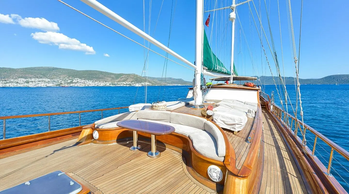 Lady Christa yacht deck with polished wood, sails up, calm blue sea sunset