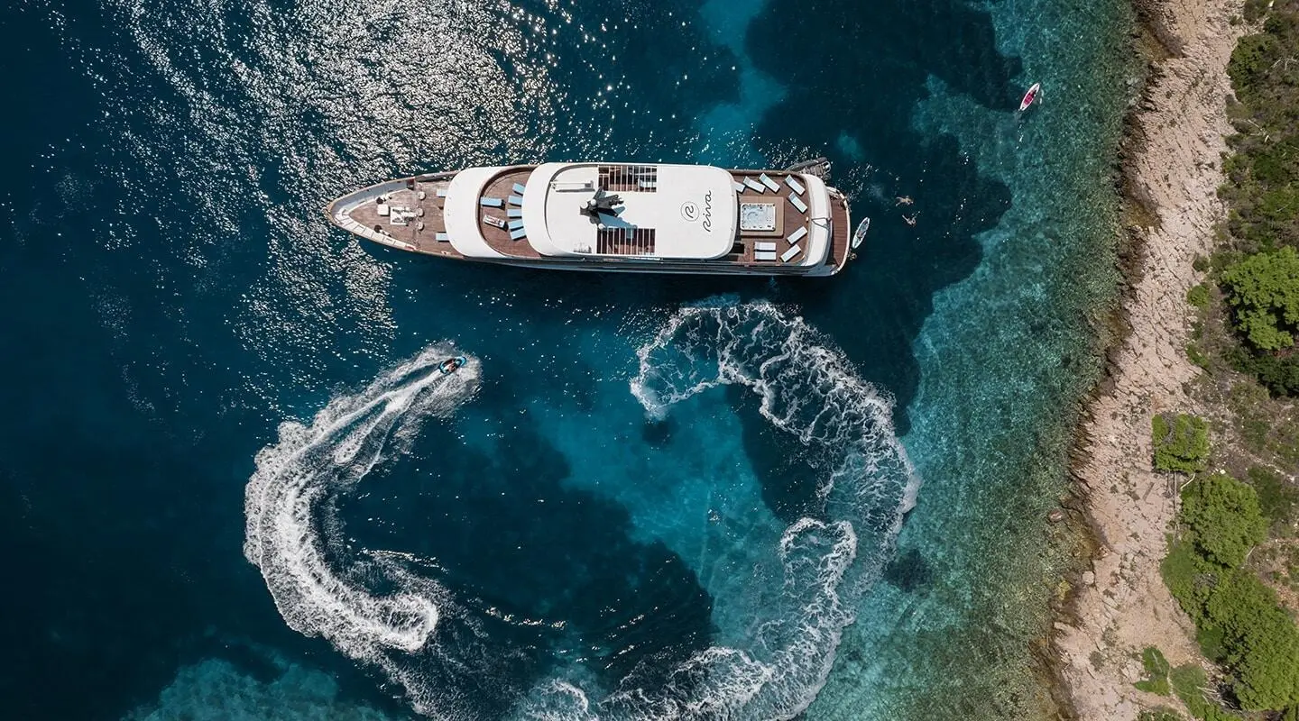 A small Riva motor yacht cruises in clear blue water from above