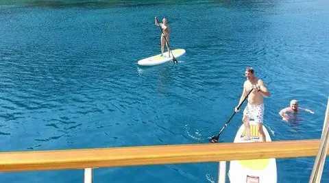 Two people on the water with a paddleboard and a kayak board in blue sea