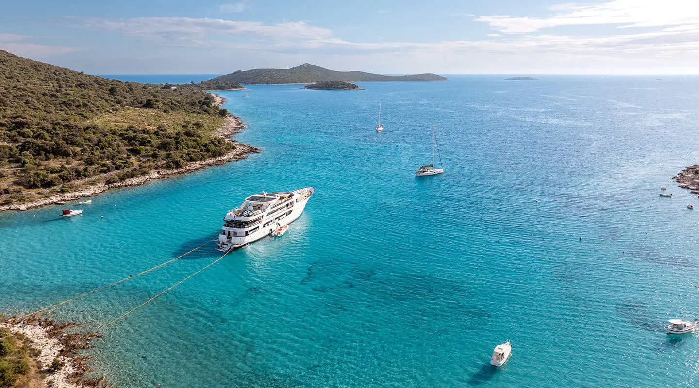 A luxury yacht named Karizma anchored in turquoise waters near a rocky coastline