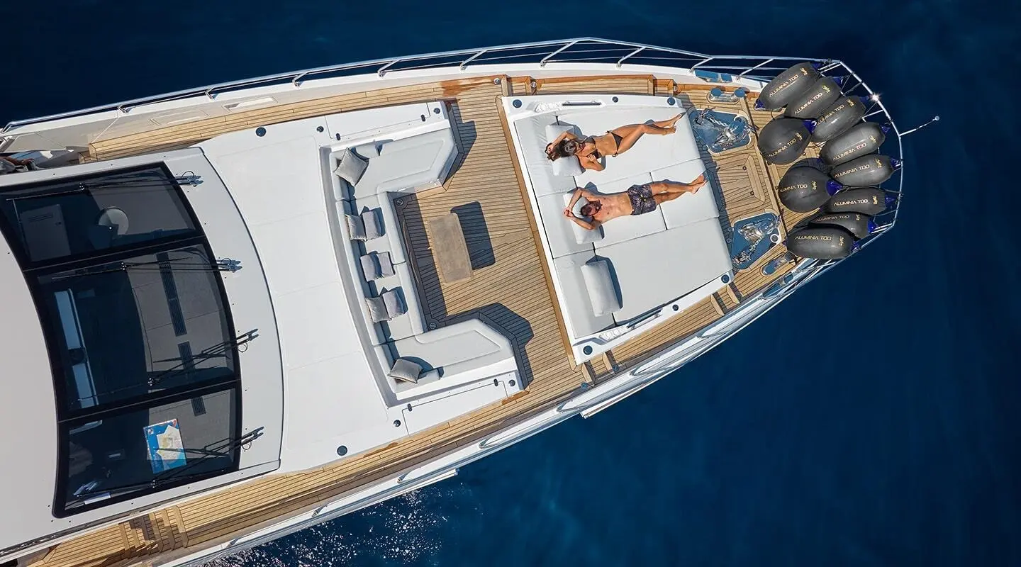 Top view of yacht deck with two people sunbathing on white loungers