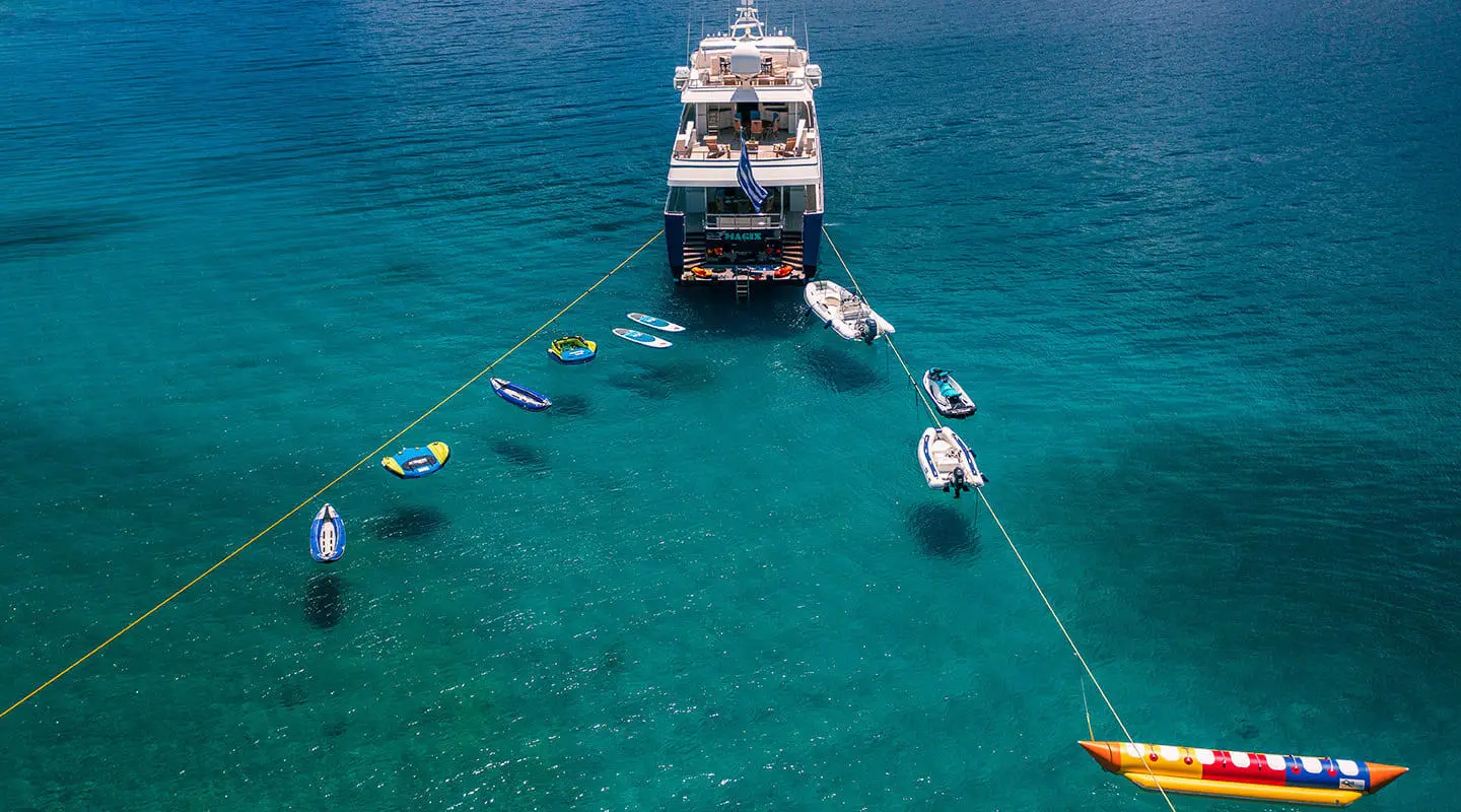 A luxurious yacht named Magix anchored in clear turquoise water near small boats