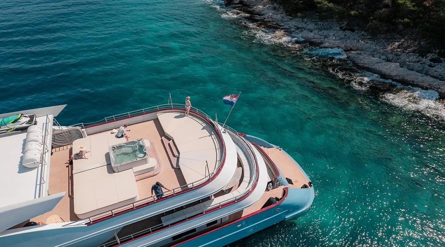 Ohana yacht anchored near rocky terrace with turquoise water and sunlit deck