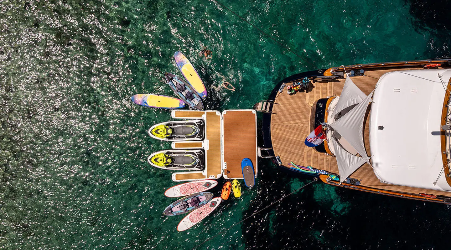 Overhead view of Dalmatino yacht anchored by clear turquoise water with guests on deck