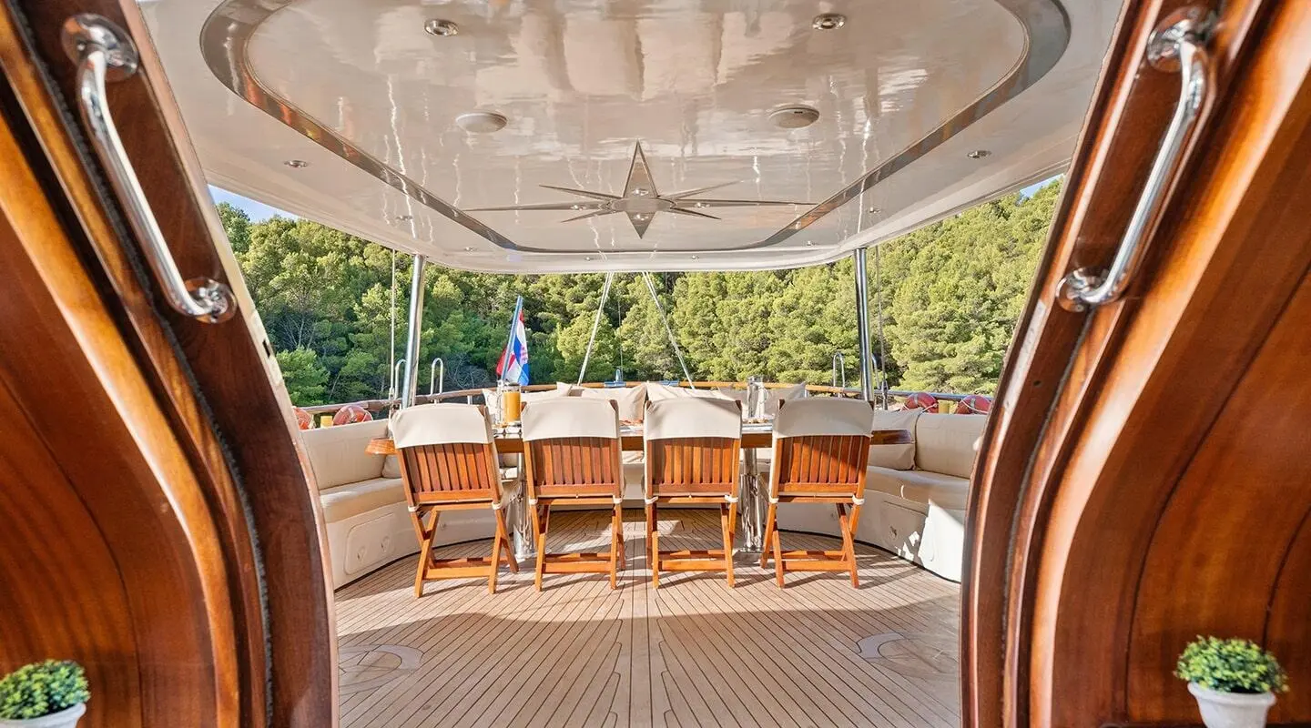 Aft deck seating and dining area on Alessandro I with wooden chairs and table.