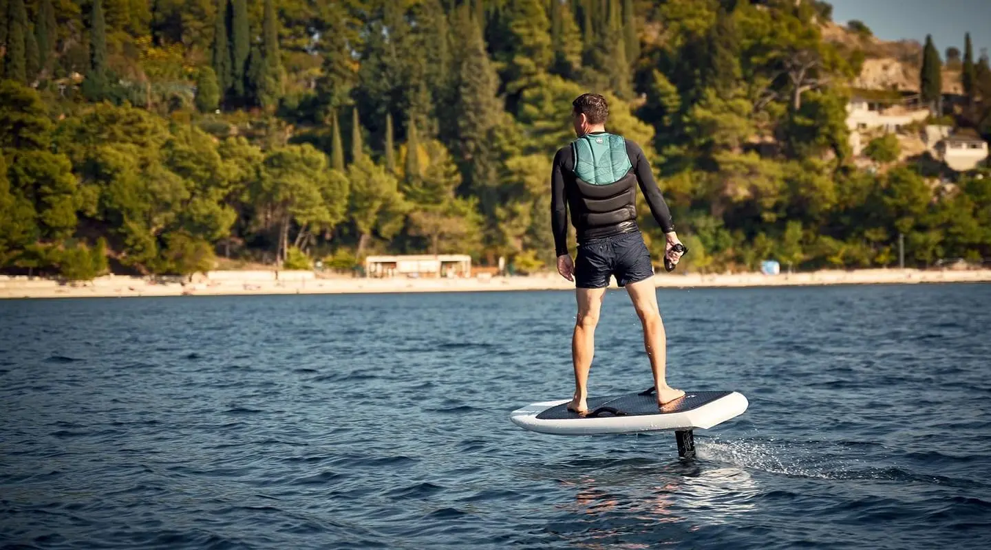 Person on a stand-up paddleboard near a forested shoreline and calm water at sunset