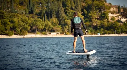 Person on a stand-up paddleboard near a forested shoreline and calm water at sunset