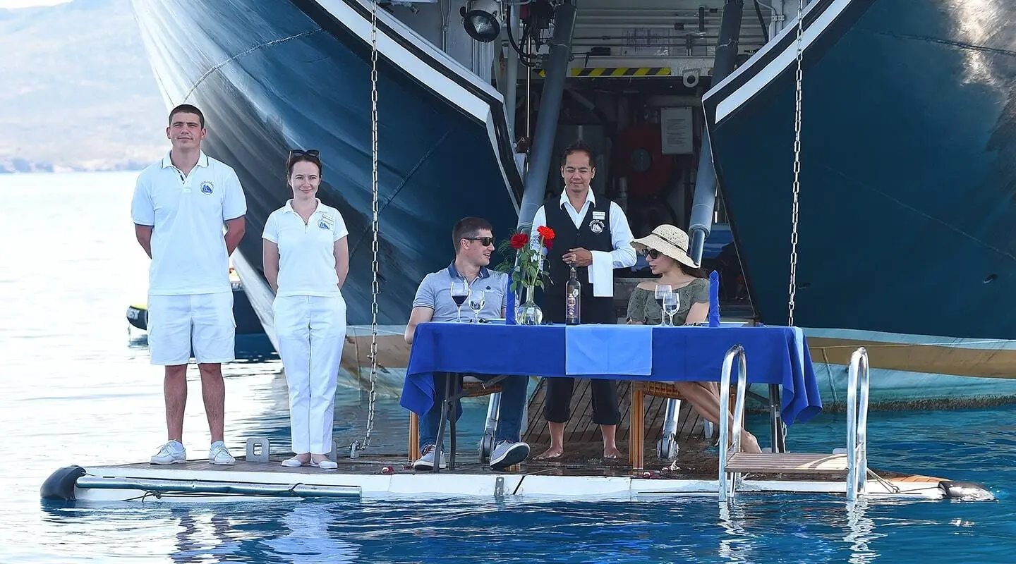 Yacht named Running on Waves with crew on deck at sunset, calm blue water