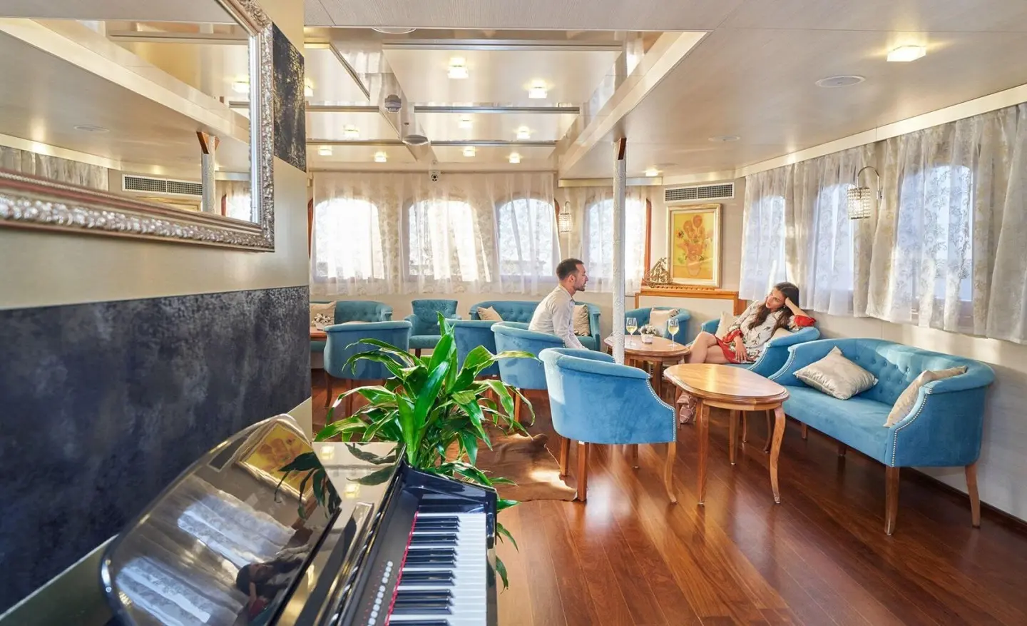 Casablanca yacht lounge area with blue chairs, wooden floor, windows, and plants